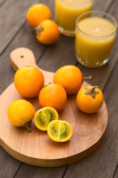 Naranjilla or Lulo fruits (lat. Solanum quitoense) on wooden board with freshly prepared naranjilla juice in the back (Selective Focus, Focus on the first naranjilla half) 
