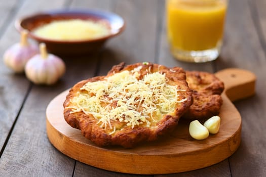 Freshly prepared traditional Hungarian deep fried flat bread called Langos made of a yeast dough, served with garlic and grated cheese (Selective Focus, Focus one third into the langos) 

 