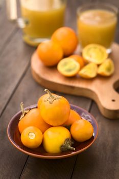 Naranjilla or Lulo fruits (lat. Solanum quitoense) in bowl with cut fruits and freshly prepared naranjilla juice in the back (Selective Focus, Focus on the naranjilla fruits in the front) 