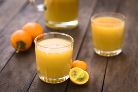 Freshly prepared juice out of Naranjilla or Lulo fruits (lat. Solanum quitoense) with fruits on the side and in the back (Selective Focus, Focus on the front rim of the glass) 