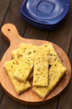 Fresh homemade garlic and cheese sticks made of a yeast dough served on wooden board, sprinkled with fresh thyme leaves (Selective Focus, Focus one third into the garlic sticks)