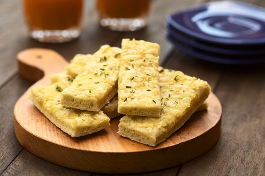 Fresh homemade garlic and cheese sticks made of a yeast dough served on wooden board, sprinkled with fresh thyme leaves (Selective Focus, Focus one third into the upper garlic stick)