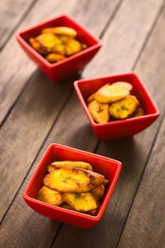 Fried slices of the ripe plantain in small red bowls, which can be eaten as snack or is used to accompany dishes in some South American countries (Selective Focus, Focus on the front of the upper plantain slice in the first bowl)