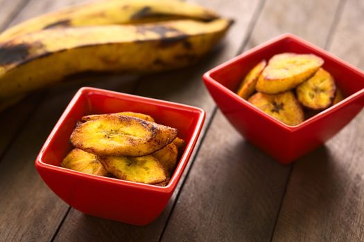 Fried slices of the ripe plantain in small red bowls, which can be eaten as snack or is used to accompany dishes in some South American countries, ripe plantains in the back (Selective Focus, Focus on the front of the upper plantain slice in the first bowl)