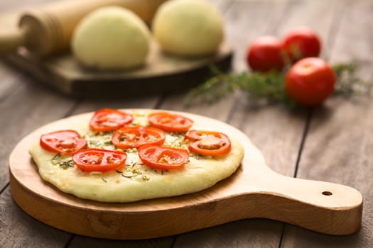 Freshly baked homemade yeast-dough flatbread topped with tomato slices, garlic and thyme leaves served on wooden board (Selective Focus, Focus on the front of the first tomato slices)  