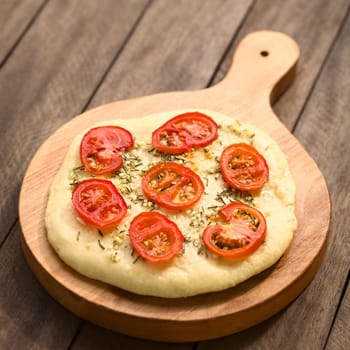Freshly baked homemade flatbread made of a yeast dough topped with tomato slices, garlic and thyme leaves served on wooden board (Selective Focus, Focus in the middle of the flatbread)  