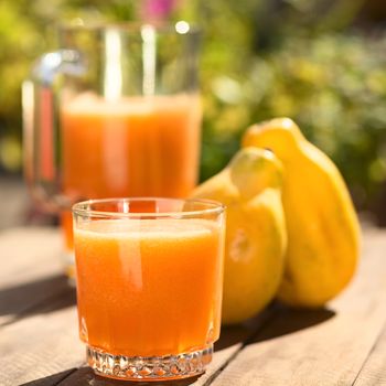 Glass of freshly prepared papaya juice with pitcher and papaya fruits in the back on table outdoors (Selective Focus, Focus on the front of the glass) 