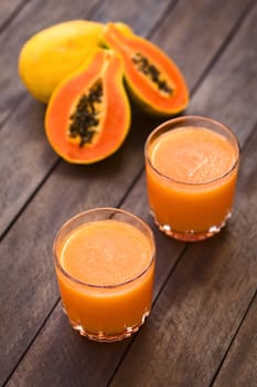 Two glasses of freshly prepared papaya juice with papaya fruits in the back (Selective Focus, Focus into the middle of the first juice) 
