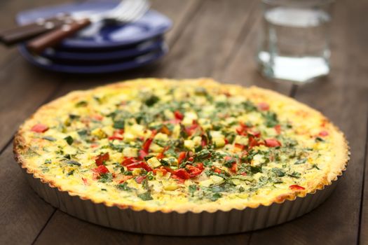 Homemade vegetarian quiche with zucchini, red bell pepper and parsley in baking dish (Very Shallow Depth of Field, Focus one third into the quiche)