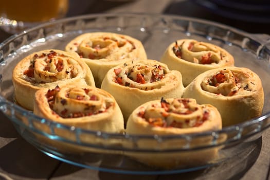 Freshly baked homemade rolls filled with tomato, ham and herbs on glass plate on outdoor table (Very Shallow Depth of Field, Focus on the middle of the middle roll) 