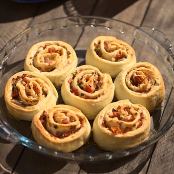 Freshly baked homemade rolls filled with tomato, ham and herbs on glass plate on outdoor table (Very Shallow Depth of Field, Focus on the middle of the middle roll) 