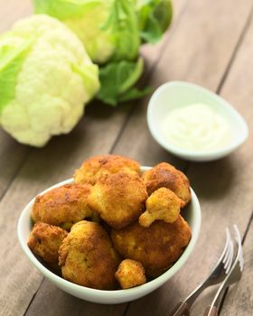 Freshly prepared breaded cauliflower in bowl with mayonnaise to dip and raw cauliflower in the back (Selective Focus, Focus on the front of the top cauliflower heads in the bowl)