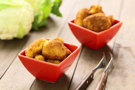 Freshly prepared breaded cauliflower in two red bowls with raw cauliflower in the back (Selective Focus, Focus on the front of the top cauliflower head in the first bowl)