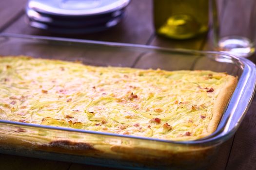 Traditional German Zwiebelkuchen or onion cake, made of a yeast dough and topped with onions and bacon in cream sauce in a glass baking pan (Very Shallow Depth of Field, Focus one third into the image) 