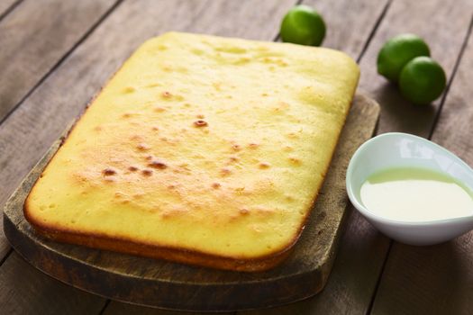 Fresh homemade key lime cake on wooden board with lime icing on the side and key limes in the back (Selective Focus, Focus one third into the cake)