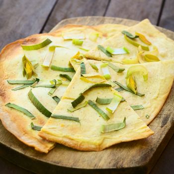 French vegetarian Tarte Flambee made of thin bread dough with a cream and leek topping, served on wooden board (Selective Focus, Focus on the upper part of the first piece)  