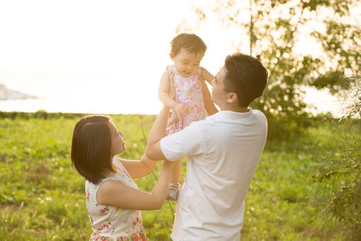 Happy Asian family playing in meadow during summer sunset, outdoors shot.