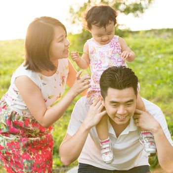 Portrait of happy Asian family playing piggyback at outdoor park during summer sunset.