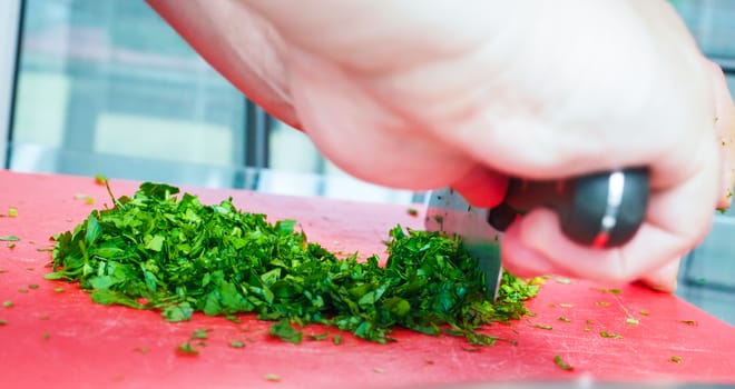 Male chef cutting parsley with big knife on red chopping board