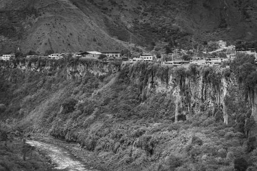 Monochrome image of the Pastaza River and the small town of Banos in Ecuador on the cliffs with some waterfalls dropping down 