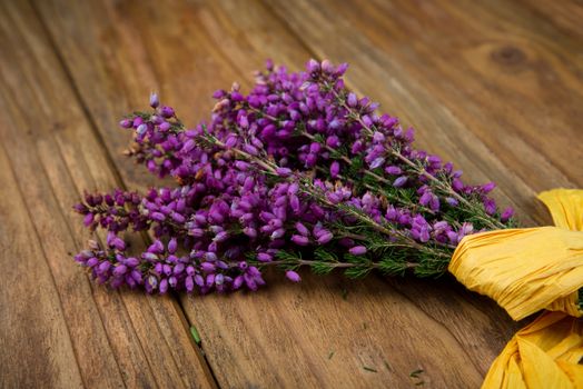 Purple and viola heather flowers on wooden table with yellow ribbon