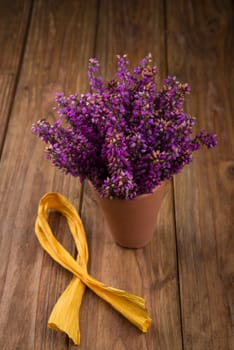 purple and viola heather flowers on wooden table in ceramic pot with yellow ribbon