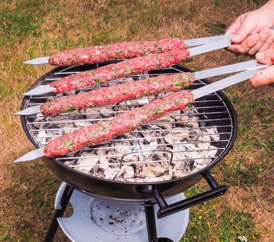 A chef putting red meat shish kebab onto a charcoal barbecue