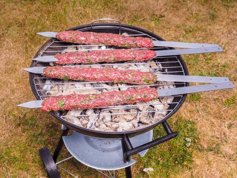 Shish kebab prepared over a black round shaped charcoal barbecue outdoors