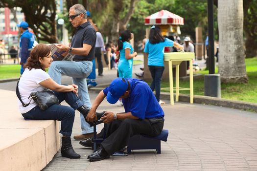 LIMA, PERU - MARCH 21, 2012: Unidentified man cleaning the shoes of an unidentified woman in Kennedy Park in the district of Miraflores on March 21, 2012 in Lima, Peru. Many people use the service of mobile shoe cleaners in Lima. 