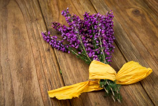 Purple and viola heather flowers on wooden table with yellow ribbon