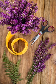 purple and viola heather flowers on wooden table in ceramic pot with yellow ribbonand scissors