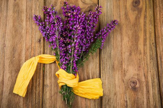 Purple and viola heather flowers on wooden table with yellow ribbon