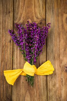 purple and viola heather flowers on wooden table with yellow ribbon