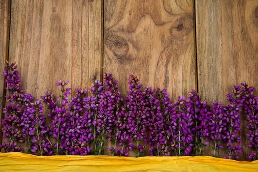 Purple and viola heather flowers on wooden table with yellow ribbon