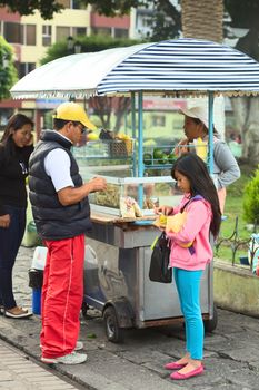 BANOS, ECUADOR - FEBRUARY 22, 2014: Unidentified people eating at snack stand selling roasted pork skin with beans (mote), tomato, onion, lime and corn at the Sebastian Acosta Park on February 22, 2014 in Banos, Ecuador.