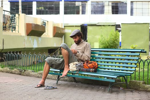 BANOS, ECUADOR - FEBRUARY 22, 2014: Unidentified young man making bracelets sitting on bench in Sebastian Acosta Park on February 22, 2014 in Banos, Ecuador. Quite a few young people in South America finance their travels by selling handicraft or making music on the streets.  