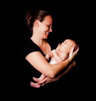 Happy smiling mother holding baby infant in arms, on black.