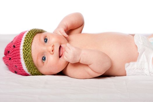 Happy smiling baby infant face with knitted watermellon hat laying on white.