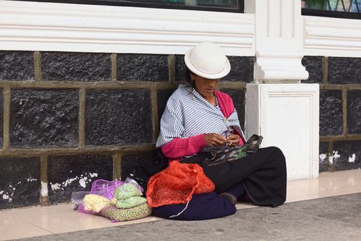 BANOS, ECUADOR - FEBRUARY 25, 2014: Unidentified woman peeling garlic and selling garlic and peas on the street sitting on the pavement on February 25, 2014 in Banos, Ecuador. 