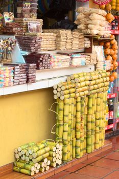 BANOS, ECUADOR - FEBRUARY 26, 2014: A small shop close to the bus terminal offering fresh sugarcane, sweets, fruits and beverages on February 26, 2014 in Banos, Ecuador. The sweets in the middle wrapped in plastic are a specialty from Banos called Melcocha, which are a kind of taffy  made of cane sugar.