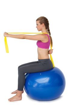 Full length of a fit young woman exercising on fitness ball over white background