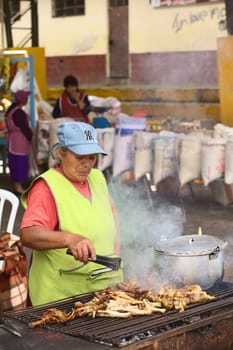 BANOS, ECUADOR - FEBRUARY 26, 2014: Unidentified woman barbecuing chicken legs for sale at the market on Plaza 5 de Junio on February 26, 2014 in Banos, Ecuador. Market days are Wednesday, Friday and Sunday, where not only fruits and vegetables are being sold but also many snacks and fast foods, fried and barbecued.