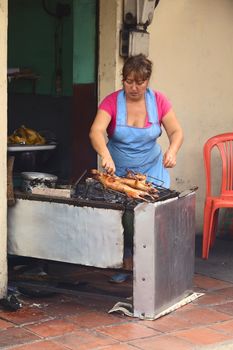 BANOS, ECUADOR - FEBRUARY 28, 2014: Unidentified woman roasting guinea pig for sale at the market hall on Ambato Street on February 28, 2014 in Banos, Ecuador. In Ecuador, guinea pig (cuy in Spanish) is considered a delicacy and is usually expensive.