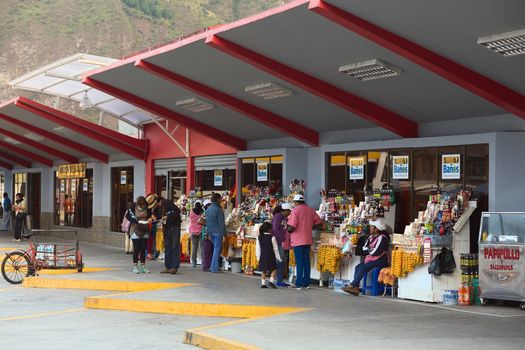 BANOS, ECUADOR - MARCH 7, 2014: Unidentified people at the bus terminal on March 7, 2014 in Banos, Ecuador. Two people are looking at a map and others are around the numerous snack stands offering sweets, fruits and drinks.