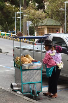 AMBATO, ECUADOR - APRIL 9, 2014: Unidentified woman with baby at a small cart filled with coconut at the roadside on Martinez Street on April 9, 2014 in Ambato, Ecuador. Ambato is the capital of the Tungurahua Province in Central Ecuador. 