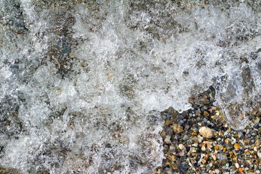 Small multi-colored sea stones on the beach, covered with transparent sea water.