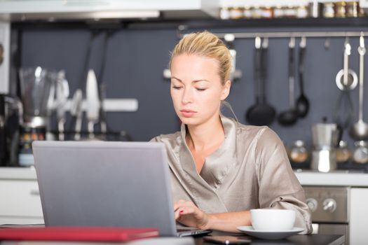 Business woman in her nightgown working remotly from her dining table in the morning. Home kitchen in the background.