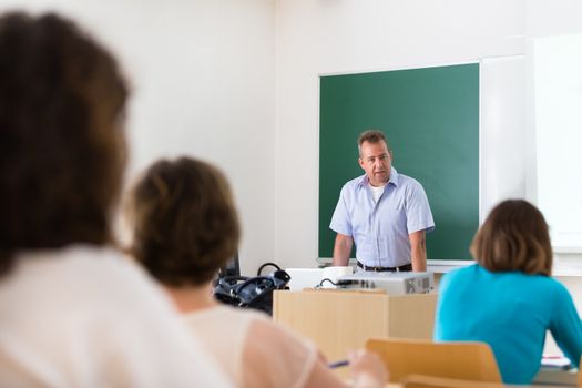 Teacher at university in front of a whiteboard screen. Students listening to lecture and making notes.