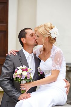 beautiful young wedding couple, blonde bride kissing her groom outdoor