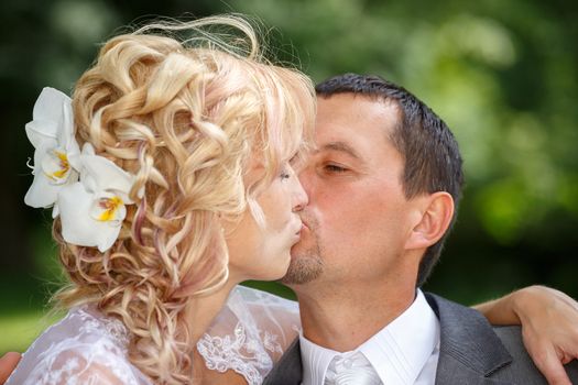 beautiful young wedding couple, blonde bride kissing her groom outdoor